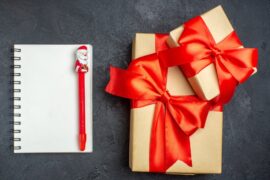 view-christmas-background-with-beautiful-gifts-with-bow-shaped-ribbon-notebook-with-pen-dark-background_-