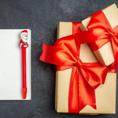 view-christmas-background-with-beautiful-gifts-with-bow-shaped-ribbon-notebook-with-pen-dark-background_-