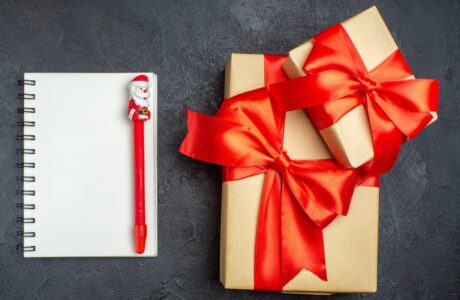 view-christmas-background-with-beautiful-gifts-with-bow-shaped-ribbon-notebook-with-pen-dark-background_-